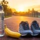 Garrafa de água, banana e par de tênis de corrida sobre pista ao amanhecer, simbolizando preparo para treino com energia.
