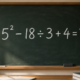 Lousa verde em sala de aula com a expressão 5² − 18 ÷ 3 + 4 = ? escrita em giz branco.