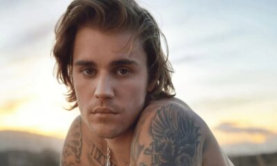 Cantor Justin Bieber sem camisa, com cabelos ondulados e tatuagens no ombro e pescoço.
