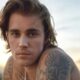 Cantor Justin Bieber sem camisa, com cabelos ondulados e tatuagens no ombro e pescoço.