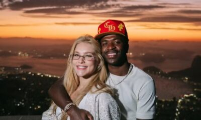 Vinicius Jr. e Virginia Fonseca sorrindo, abraçados, com a cidade do Rio de Janeiro e pôr do sol ao fundo
