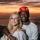 Vinicius Jr. e Virginia Fonseca sorrindo, abraçados, com a cidade do Rio de Janeiro e pôr do sol ao fundo