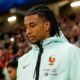 Jogador Michael Olise com dreads, jaqueta azul clara com logotipo da França e patrocinadores