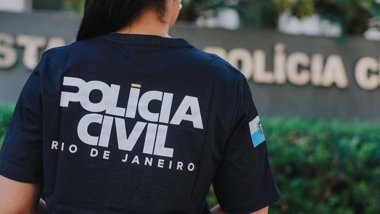 Costas de uma pessoa vestindo camiseta da Polícia Civil do Rio de Janeiro com emblema