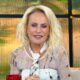 Apresentadora Ana Maria Braga sorrindo com cabelo loiro e maquiagem, exibindo "11:47 Curitiba" na tela