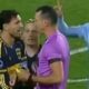 Árbitro de roxo, dois jogadores azul-amarelo e um azul-claro discutem acaloradamente em campo