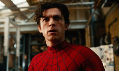 Tom Holland como Homem-Aranha, rosto sério, vestindo traje vermelho e preto em ambiente interno
