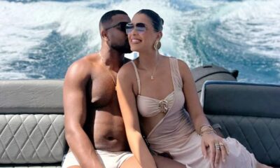 Homem beija a bochecha de mulher sorridente com óculos de sol em barco em movimento