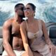 Homem beija a bochecha de mulher sorridente com óculos de sol em barco em movimento