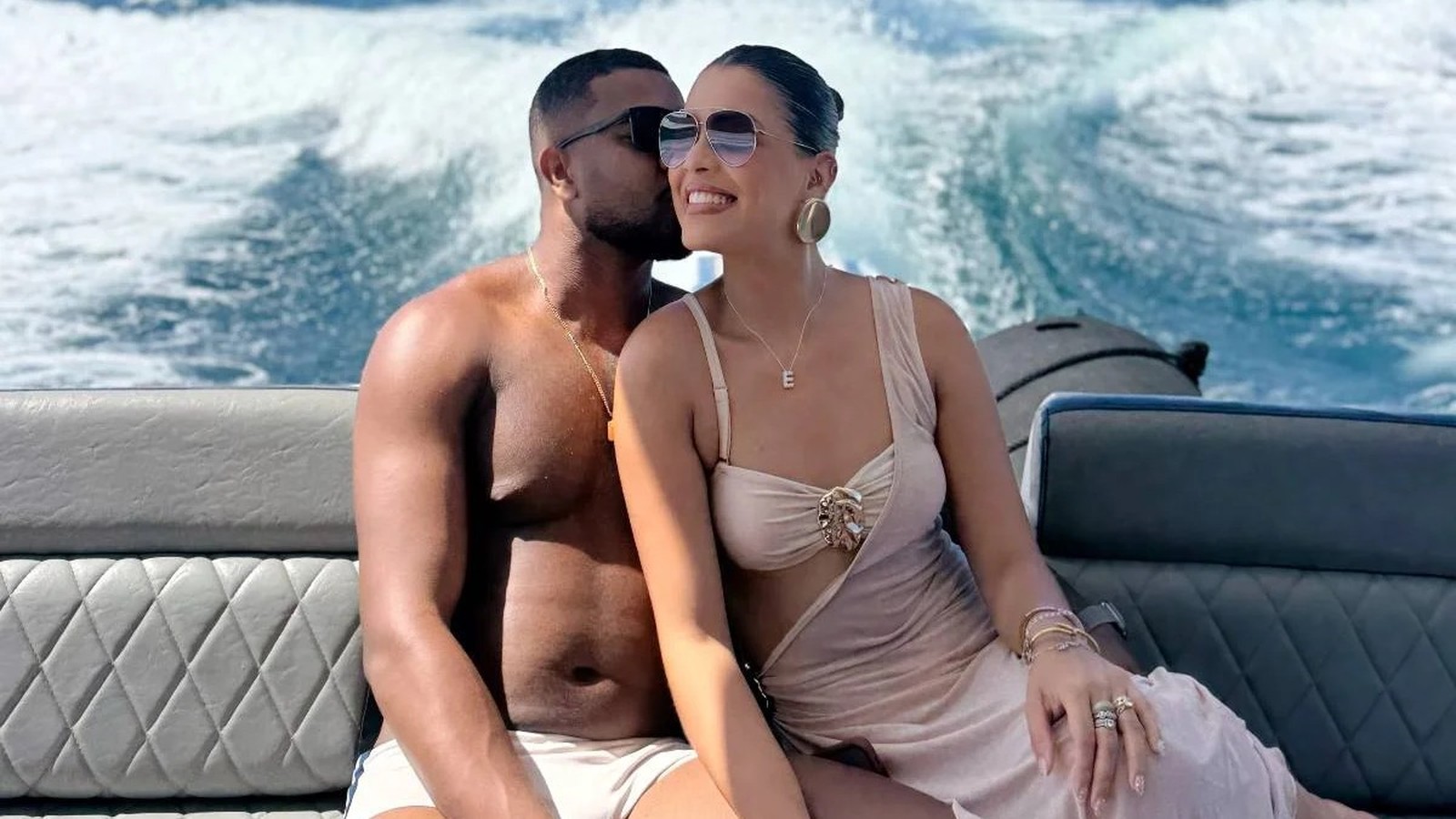 Homem beija a bochecha de mulher sorridente com óculos de sol em barco em movimento