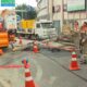 Trabalhadores perto de árvore caída, poste, fios, cones e fita 'PERIGO AFASTE-S' na rua