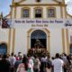 Igreja da Paróquia Nosso Senhor dos Passos, em Rio Preto (MG), com a imagem do Senhor Bom Jesus dos Passos na entrada, faixas da festa e fiéis reunidos para a celebração religiosa.