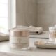 Frasco de hidratante facial ao lado de um espelho sobre uma bancada de banheiro, com destaque para ingredientes como ácido hialurônico e ceramidas, representando cuidados diários para pele madura