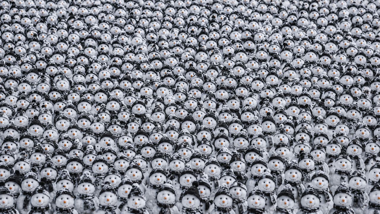 Multidão de bonecos de neve com gorros e cachecóis escuros, entre os quais há um único panda parcialmente camuflado.