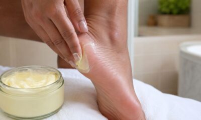 Pessoa aplica manteiga corporal vegetal no calcanhar ressecado, com pote de manteiga de ucuuba ao lado, em banheiro simples e iluminado