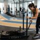 Trenó de Hyrox em academia com pista de corrida e relógio esportivo representando 120 dias de treino híbrido
