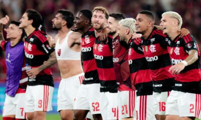 Jogadores do Flamengo em campo, comemorando a vitória. Um jogador usa um top esportivo branco