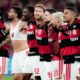 Jogadores do Flamengo em campo, comemorando a vitória. Um jogador usa um top esportivo branco