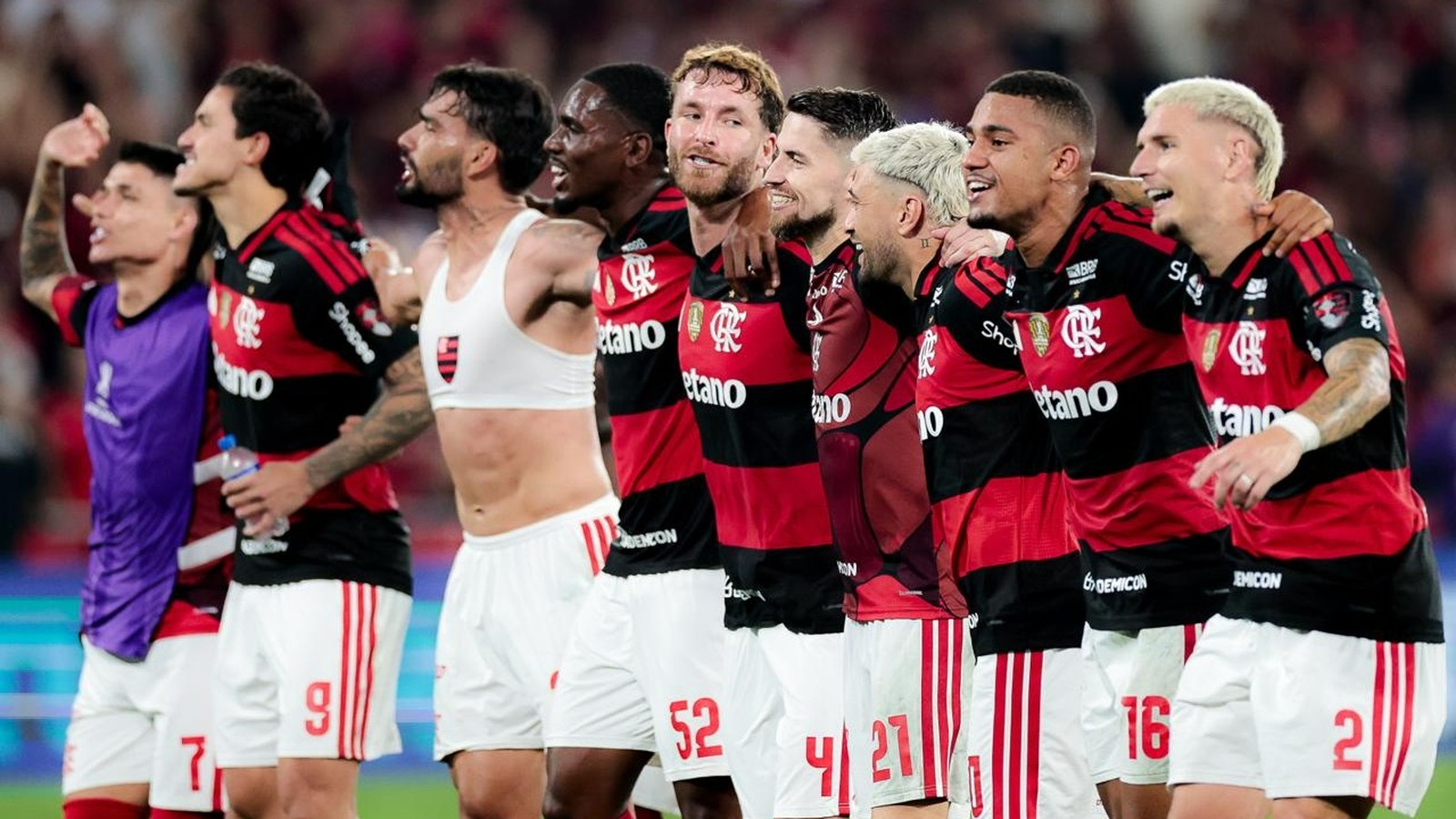 Jogadores do Flamengo em campo, comemorando a vitória. Um jogador usa um top esportivo branco