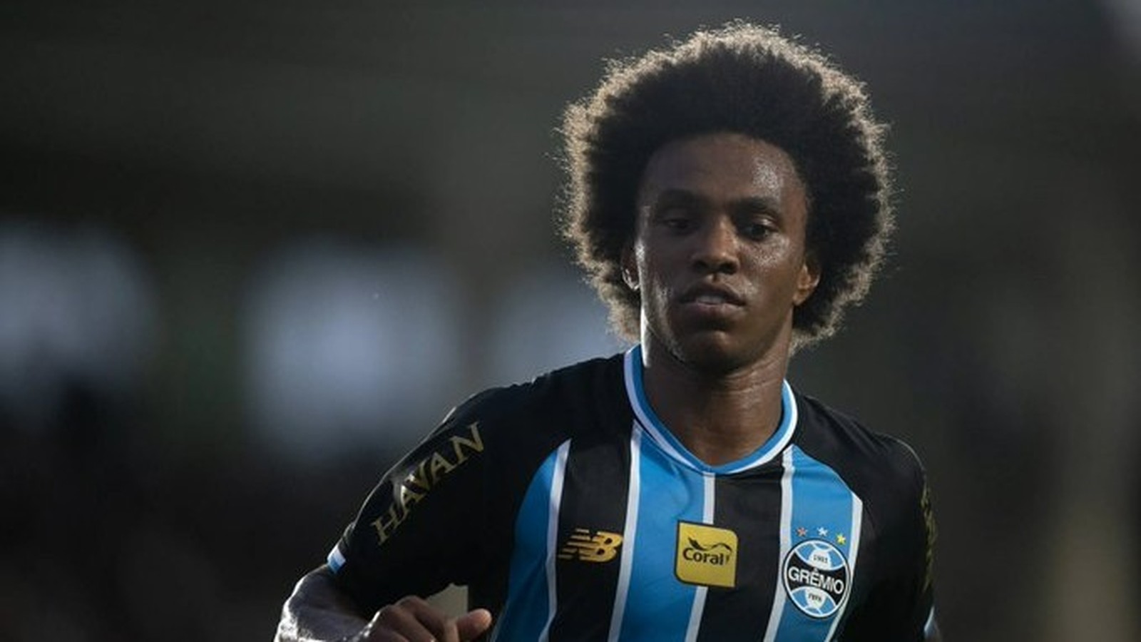 Homem de cabelo crespo e camisa do Grêmio com listras pretas e azuis