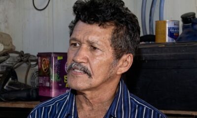 Homem de meia-idade com cabelo escuro encaracolado, bigode, camisa listrada azul e branca