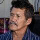 Homem de meia-idade com cabelo escuro encaracolado, bigode, camisa listrada azul e branca