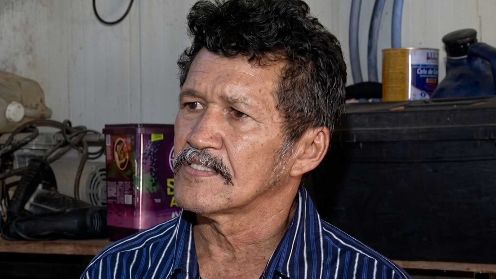 Homem de meia-idade com cabelo escuro encaracolado, bigode, camisa listrada azul e branca