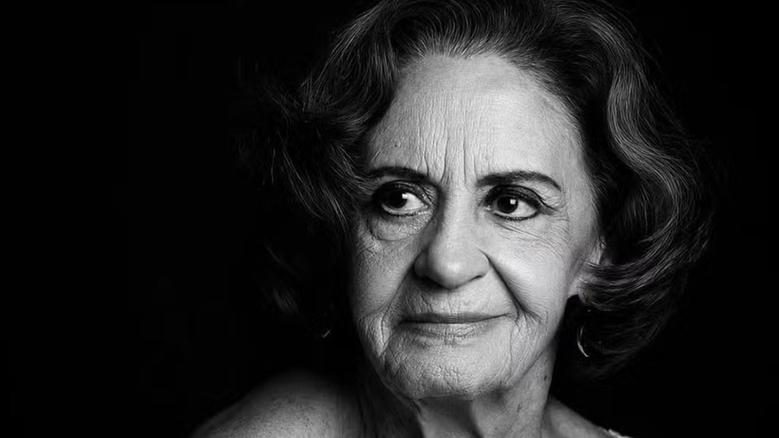 Retrato em preto e branco de uma mulher idosa com cabelo ondulado olhando para o lado