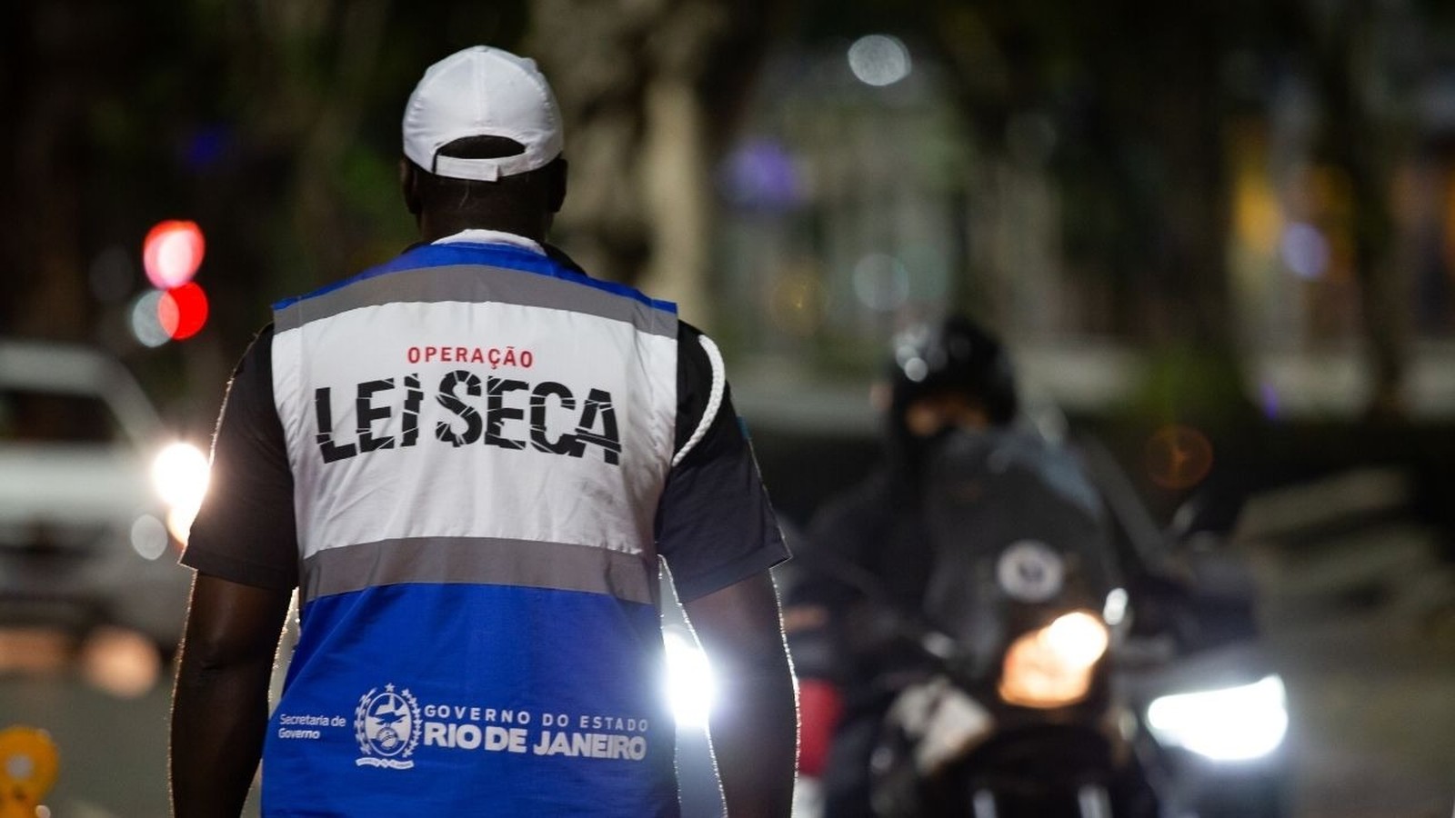 Agente de fiscalização noturna com colete "LEI SECA" e logo do Governo do Rio