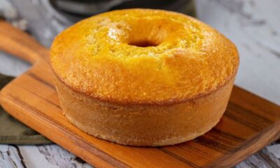 Bolo de fubá dourado em forma de anel, sobre uma tábua de madeira rústica