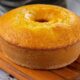 Bolo de fubá dourado em forma de anel, sobre uma tábua de madeira rústica