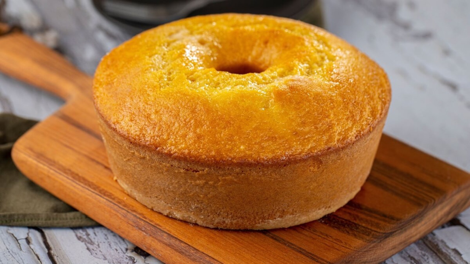 Bolo de fubá dourado em forma de anel, sobre uma tábua de madeira rústica