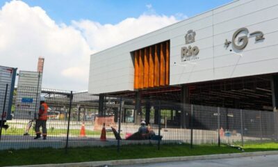 Edifício moderno branco com logo 'Rio Prefeitura' e G2, cerca, trabalhador e caminhão à frente