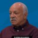 Homem idoso, bigode grisalho, camisa bordô, fundo azul. Logos "SPORTV" e texto "À ESPERA DE ALMADA"