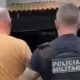Policial militar com 'POLICIA MILITAR' na camisa escolta homem em camiseta laranja