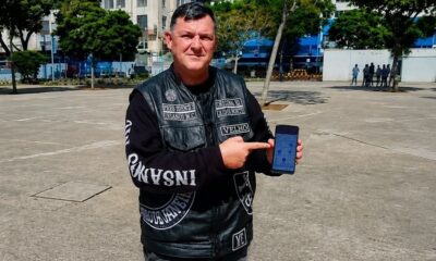 Homem com colete de couro Insanos MC aponta para smartphone com aplicativo na tela