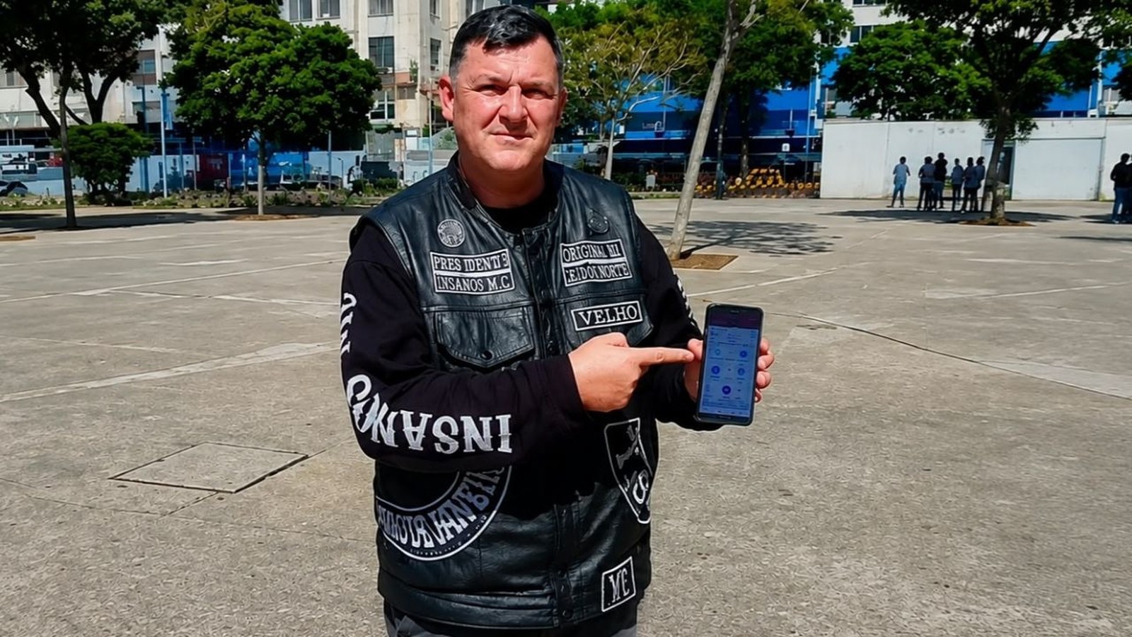 Homem com colete de couro Insanos MC aponta para smartphone com aplicativo na tela