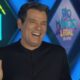 Celso Portiolli sorrindo e gesticulando com logo Domingo Legal no fundo