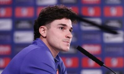 O jogador Julián Álvarez com cabelo escuro e camisa azul-arroxeada, sentado com um microfone à frente