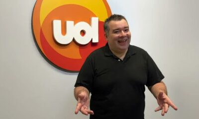 Homem sorridente gesticula à frente de logo UOL branco com círculos coloridos