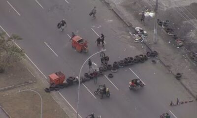 Vista aérea de rua bloqueada por fileiras de pneus e dois contêineres vermelhos com pessoas