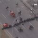Vista aérea de rua bloqueada por fileiras de pneus e dois contêineres vermelhos com pessoas