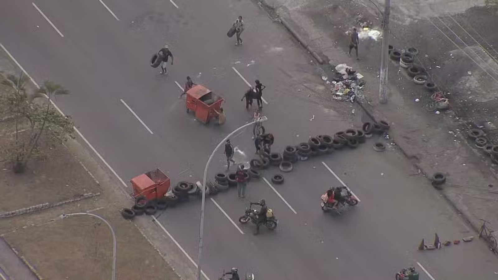 Vista aérea de rua bloqueada por fileiras de pneus e dois contêineres vermelhos com pessoas