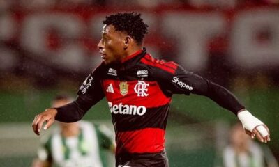 Jogador Gonzalo Plata em campo, camisa Flamengo preta e vermelha, logos, bandagem branca no pulso