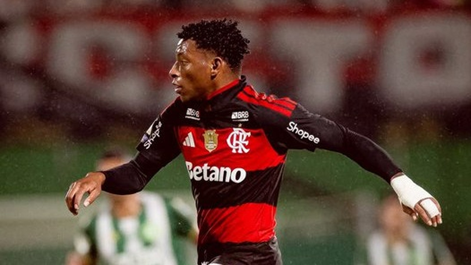 Jogador Gonzalo Plata em campo, camisa Flamengo preta e vermelha, logos, bandagem branca no pulso
