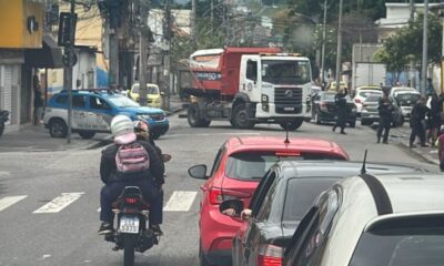 Rua em Cascadura com carro da Polícia Militar, caminhão, motos, carros e policiais.