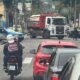 Rua em Cascadura com carro da Polícia Militar, caminhão, motos, carros e policiais.