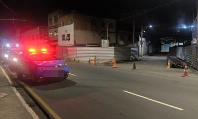 Duas viaturas policiais com luzes de emergência em rua escura com cones e cercas