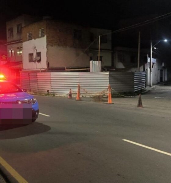 Duas viaturas policiais com luzes de emergência em rua escura com cones e cercas
