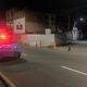 Duas viaturas policiais com luzes de emergência em rua escura com cones e cercas